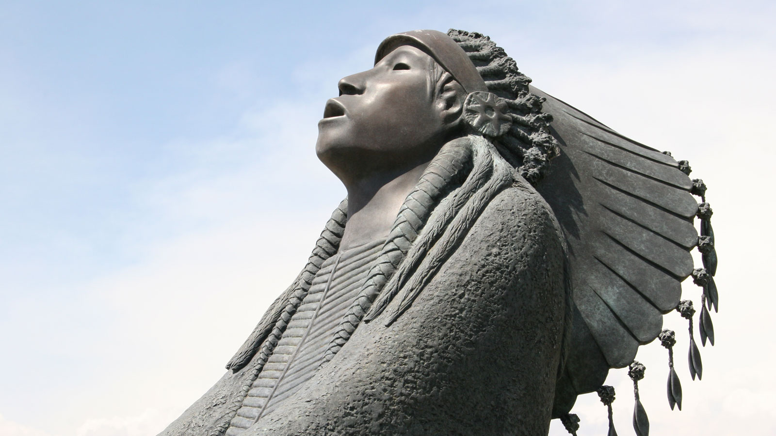 A sculpture of a Native American in traditional attire with head tilted back.
