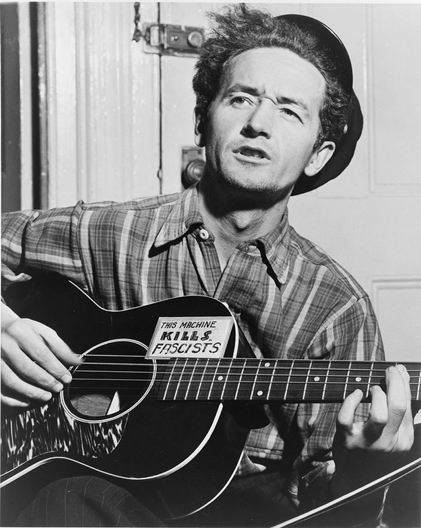 A vintage black and white photo of a man playing a guitar and singing.
