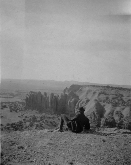 A man sits on the edge of a cliff and looks out over the landscape.