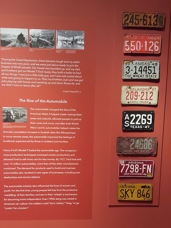 A close up of part of the Route 66 exhibition featuring a row of vintage license plates mounted to a rust red wall.