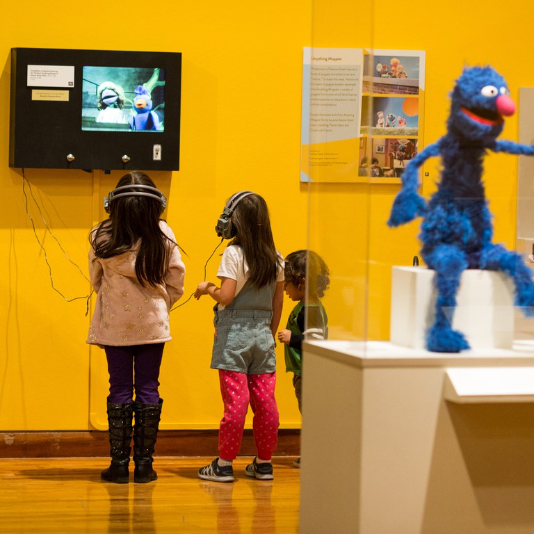 Three small children watch a video at the Jim Henson muppets exhibition.
