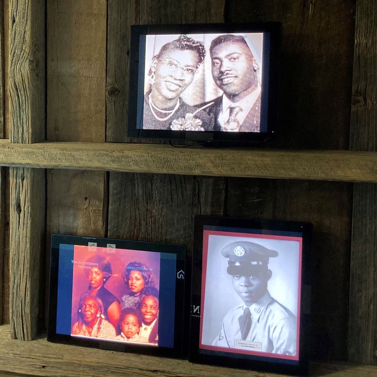 A wooden bookshelves holding three digital photo displays with photos of smiling Black families.