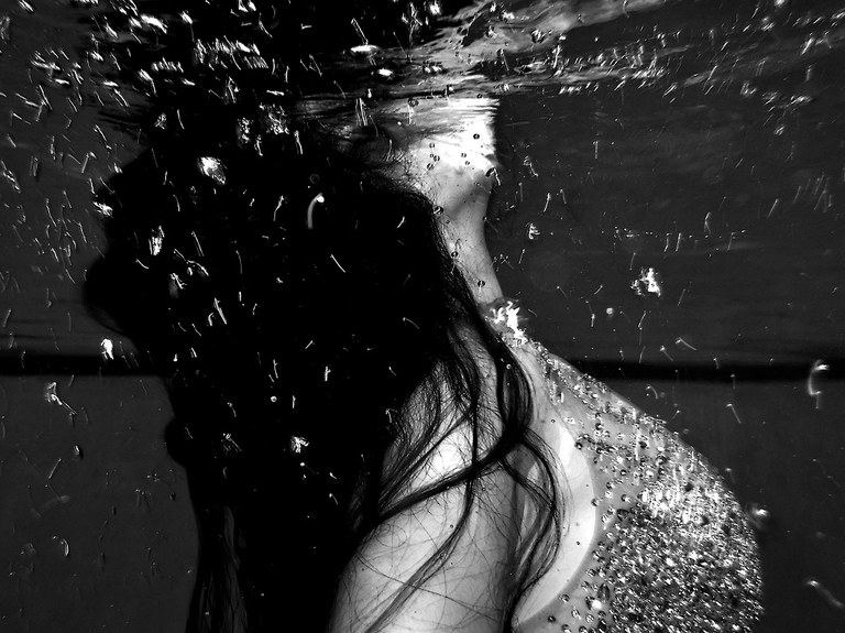 A photography by Isaiah Sisneros called "Swim" featuring a close up of a woman surfacing for air from the underwater perspective.