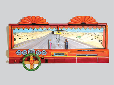 Carved depiction of a view from the driver's and passenger's seat of a car made of bright orange panted wood. Inside the orange framed windshield is a painted image of the road. The rearview mirror contains a triangle with an eye in the center and a rosary hanging below. Two carved figures sit on the dashboard under the rearview mirror. The steering wheel is depicted as a crown of thorns-the thorns made up of nails and in the center of the wheel is a flaming heart.