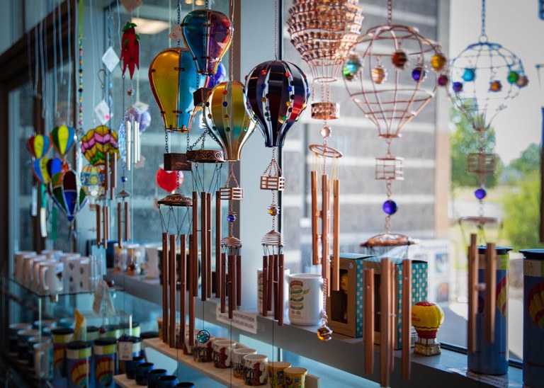 A portion of the Balloon Museum Shoppe looking out through a window with various hot air balloon window hangs and wind chimes on display.