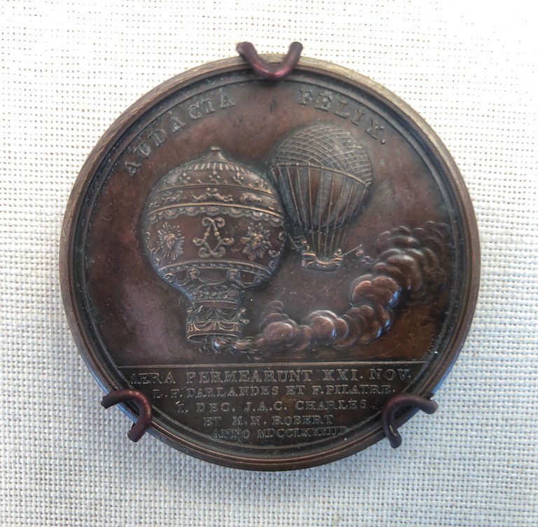 A metal medallion featuring reliefs of two hot air balloons and text about the first manned flights.