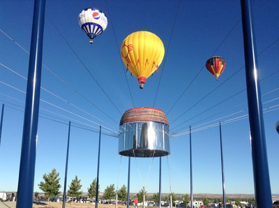 The 3D metal sculpture, Sky Portal, which is a representation of the burner part of a hot air balloon. Hot air balloons rise in the sky in the background.