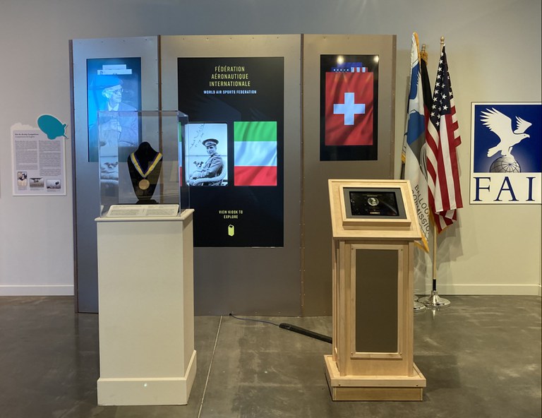 A portion of the Hall of Fame exhibition featuring a digital display, a display case with a medal, and a podium with a plaque.