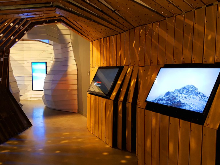 A view from within the Precipitation Pod in the Weather Lab exhibition, facing two digital interactive displays inside a tunnel-like walkway.