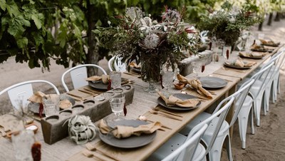 A decorated and set long table with lush greenery in the background.