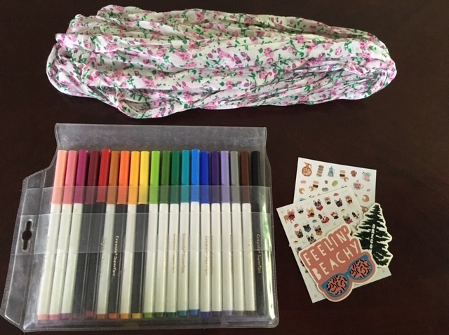 An overhead view of a packaged of colored markers, a piece of fabric, and stickers.