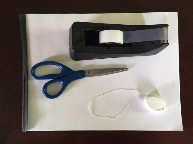 An overhead view of a pair of scissors, a tape dispenser, and a roll of floss.