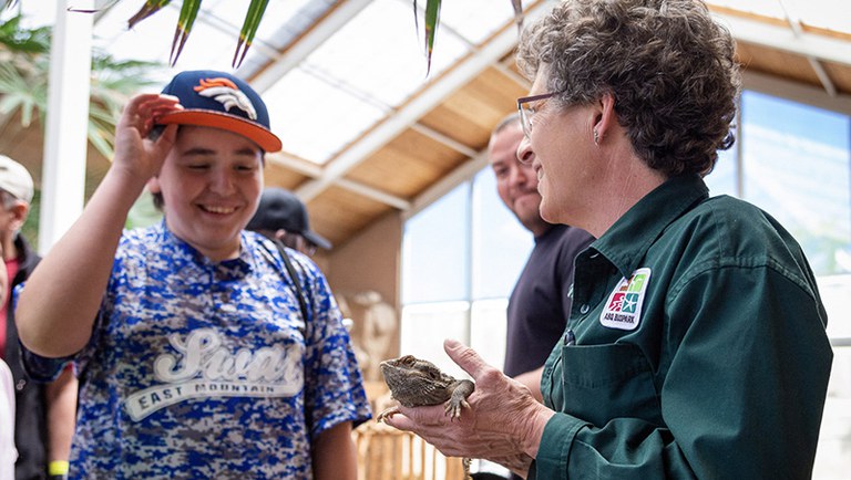 A child smiles at a lizard being held by a BioPark staff member.