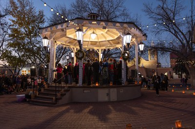 A group of people standing on a well lit gazebo at night.