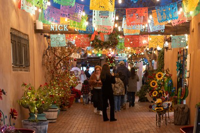 People walking under colorful banners hung between two buildings.