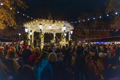 A large crowd standing around a well lit gazebo decorated for Christmas.