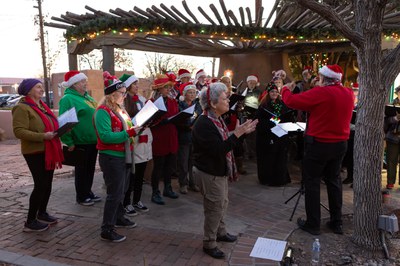 Carolers singing outside next to an adobe building.