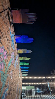 Multi-colored, acrylic hands installed on the side of a brick building.