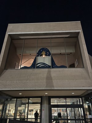 Window installation of a figure with blue hair reading a book. Their face is lit up with lights. 