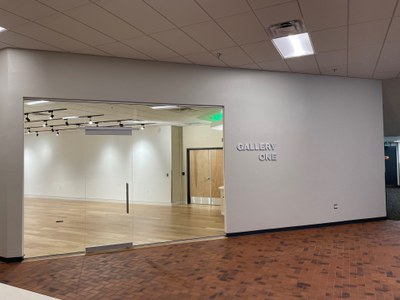 View into Gallery One from the first floor of the City Hall building. A wall of windows to the left and a blank wall to the right.