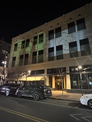 Cartoon drawings of people's faces projected onto the side of the Rosenwald Building at night.