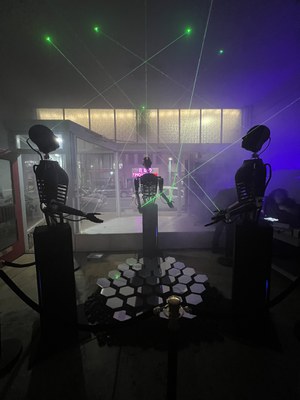 A group of three 3-D printed robots positioned around mirrored hexagons with green lasers projecting from the robots.