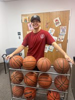 Staff in red shirt standing behind rack of basketballs