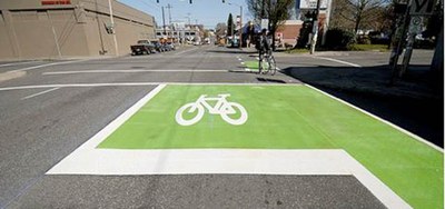 Shows a green bicycle box with a white bike symbol in the middle of the box area. 