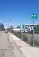 There is a street with vehicle parking on both sides of the street and there is a sign with a bicycle symbol that says bike route.