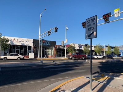 Shows the pedestrian hybrid beacon or HAWK signals on Central Ave. in Nob Hill. There is a crosswalk for people walking to cross the street to a pedestrian refuge island in the center of the street. There is a sign that says "Stop Here on RED" indicating where drivers must stop when the sign is activated.