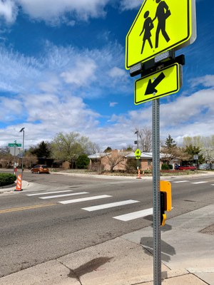 There is a rectangular rapid flashing beacon (RRFB) with a bright yellow sign of people walking and an arrow pointing down to a crosswalk. There is a button on the RRFB for people to activate the signal.