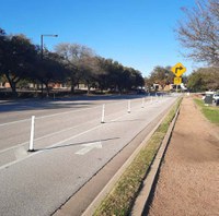 There is a bike lane with a striped buffer space between the bike lane and where people drive automobiles. Within the striped buffer space there are white, reflective posts mounted, which would discourage people driving from driving in the bike lane.