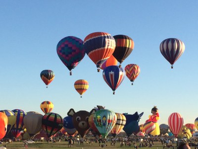 A filed full of colorful hot air balloons. Some are on the ground and some are in the air.