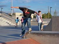 Teenagers skate boarding and 2 young children wearing helmets walking.