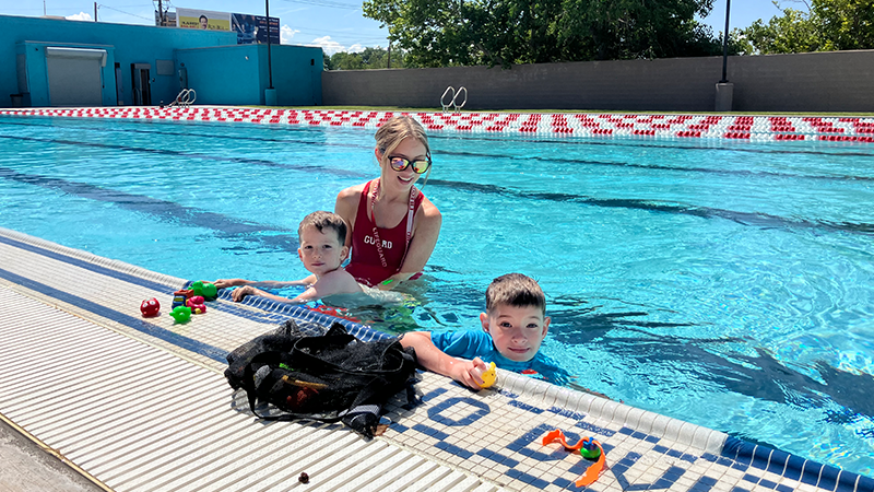 A lifeguard with 2 children in a pool by the edge.