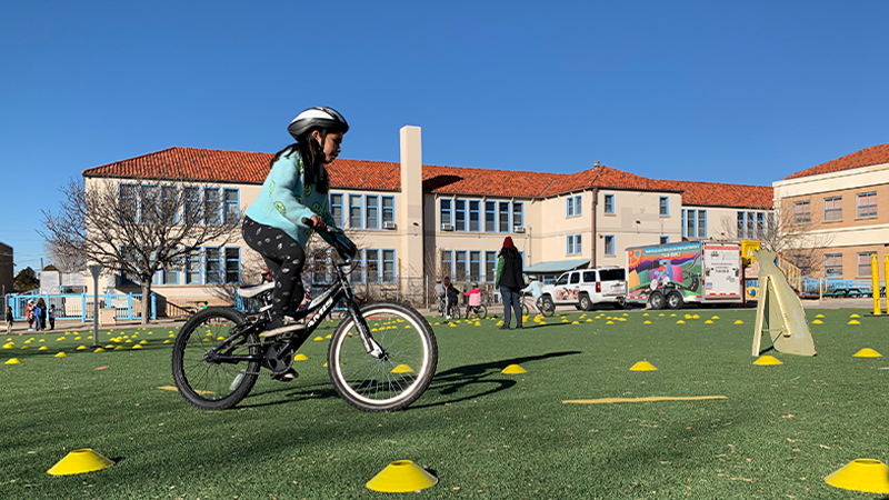 A child wearing a helmet, riding a bike around a course made of yellow cones.