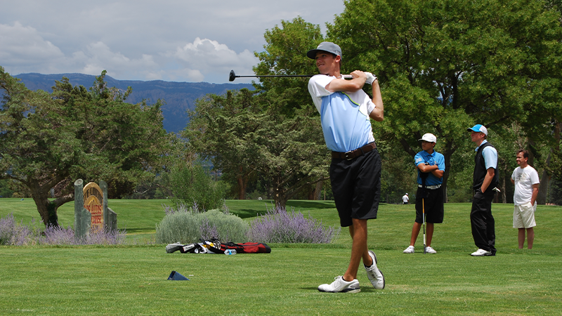 A man swinging a golf club as others watch.