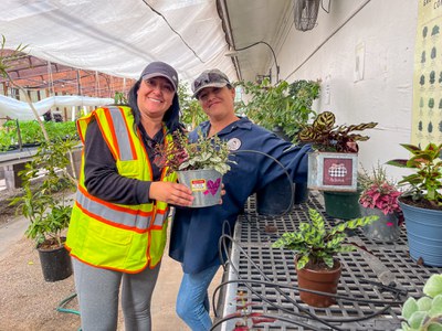 Two volunteers posing while holding plants in small metal pots.