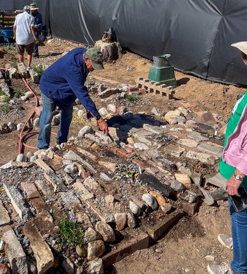 A volunteer digs in a rock garden as another volunteer watches and 2 more work in the background.