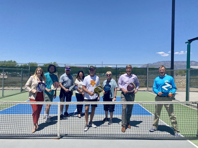 Mayor Keller, Director Simon, and others posing with pickleball paddles on a pickleball court.