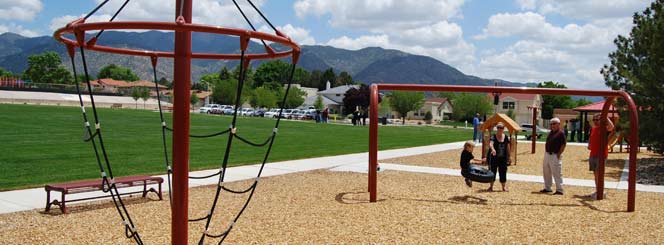 A family on a playground next to a green sports field.