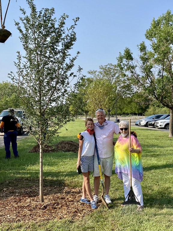 Three people posing next to a tree they just planted in a park.