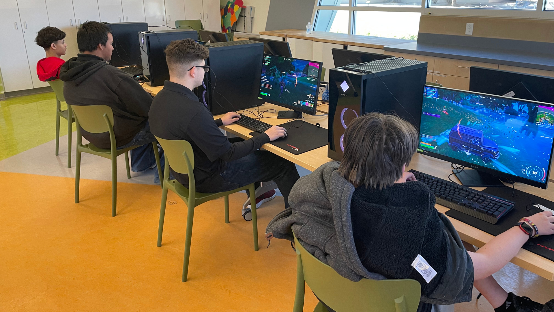 A group of gamers at a row of computers, playing Fortnite.