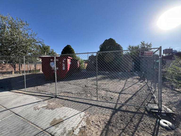 A dilapidated house in need of repair. There is a temporary chain link fence installed around the perimeter of the property.