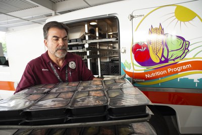 A man holding a tray of prepackaged meals in front of a Nutrition Program truck.