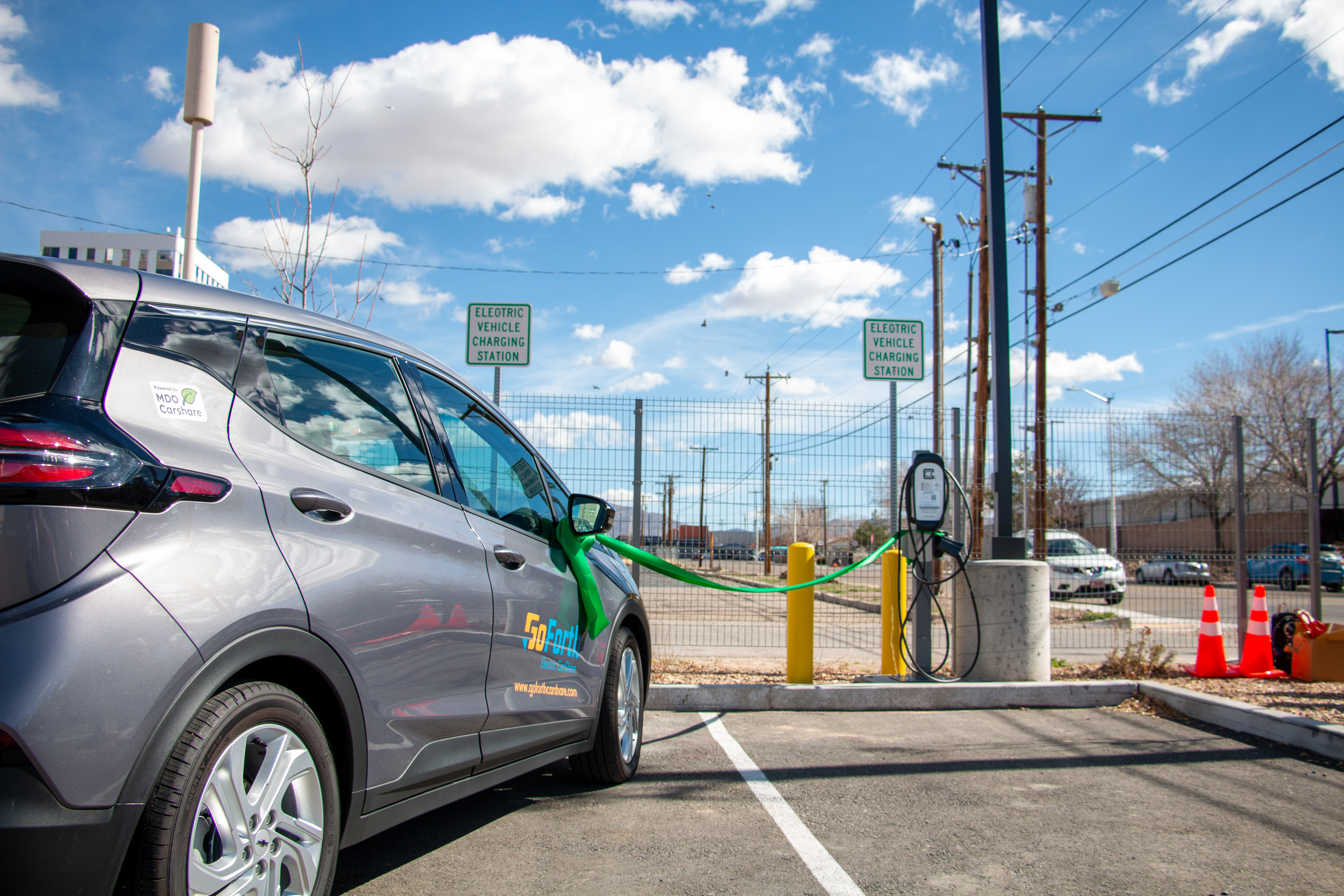 A gray electric vehicle parked next to and plugged into a charging station.