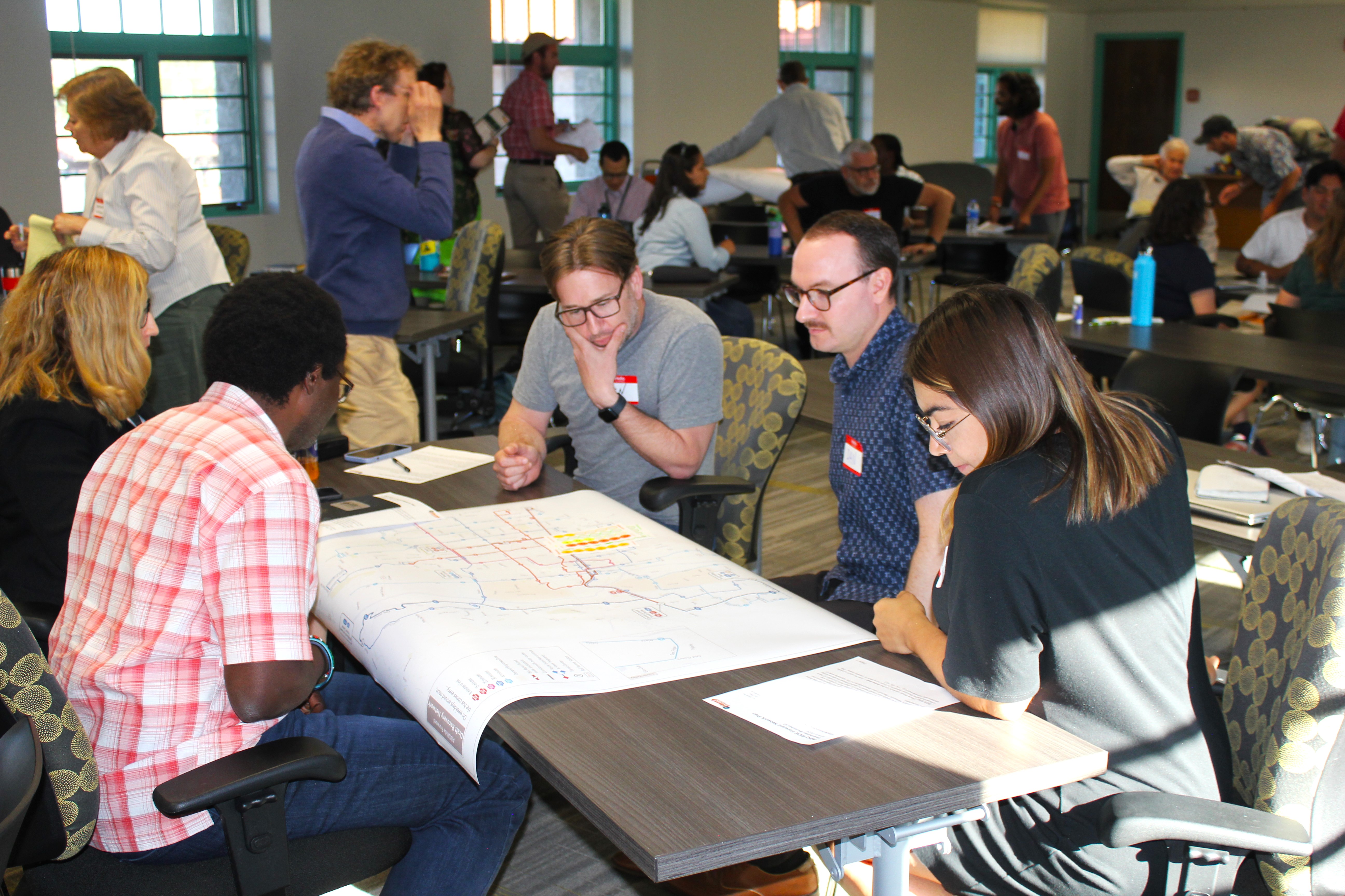 A group of five diverse people sitting at a table looking at a map.